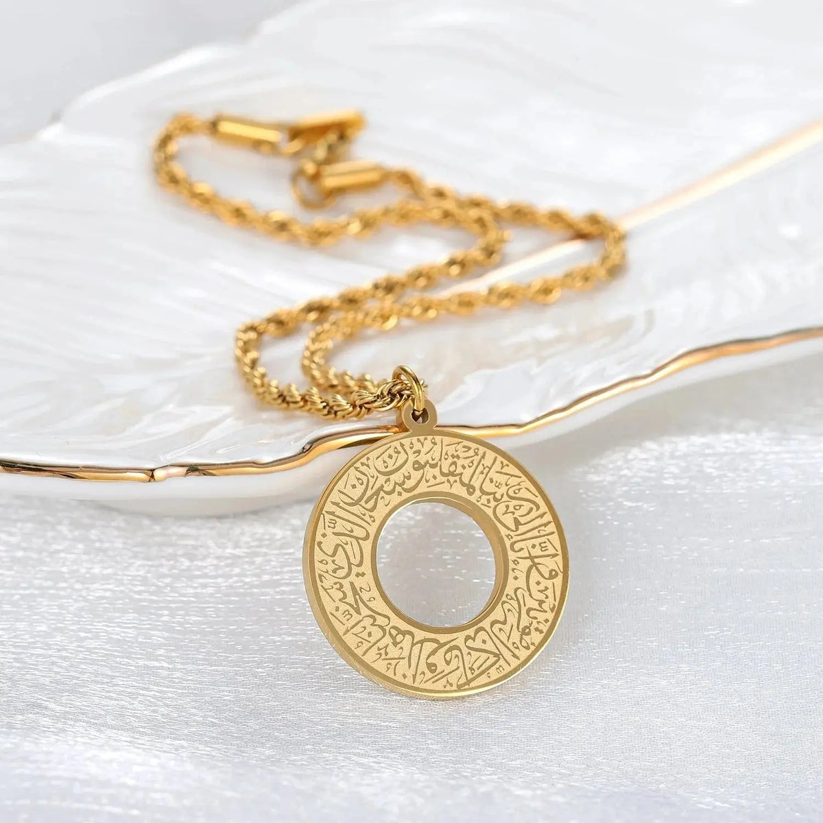 Gold circular pendant necklace with intricate Arabic calligraphy on a white tray.