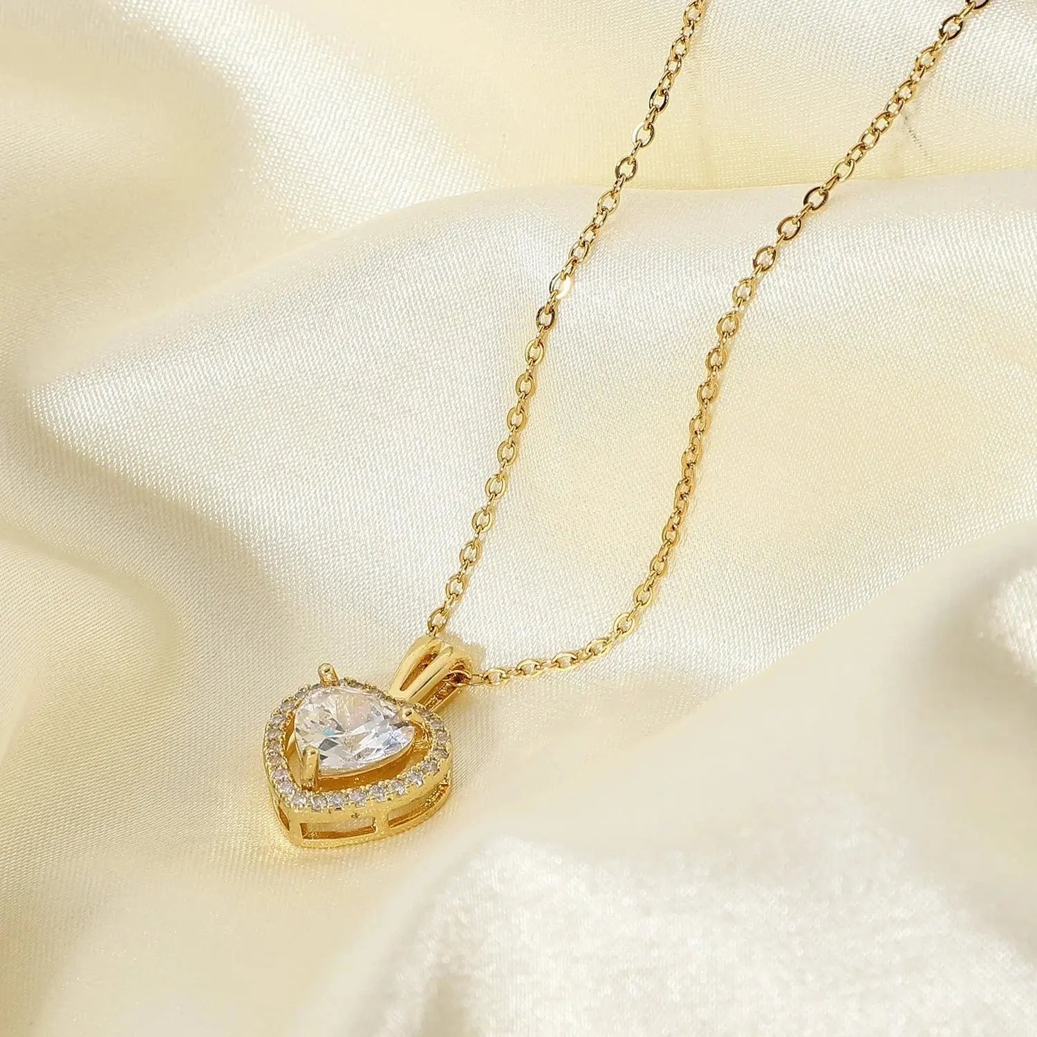 Gold heart-shaped pendant necklace with a sparkling clear stone on cream satin fabric