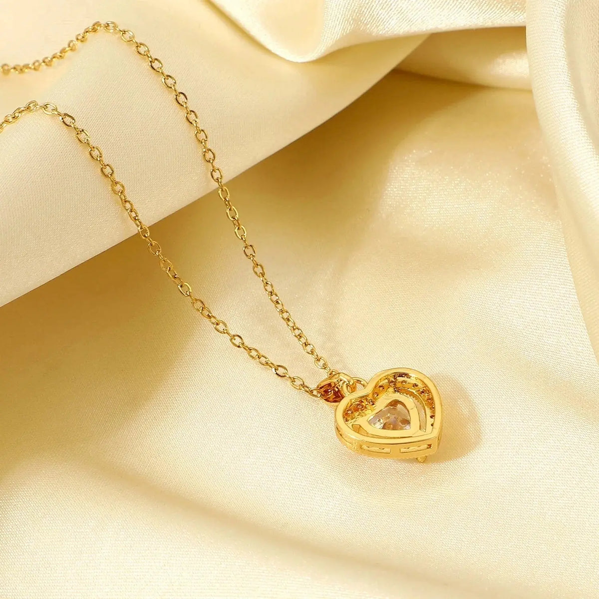 Gold heart-shaped pendant necklace with a sparkling center stone on cream satin fabric